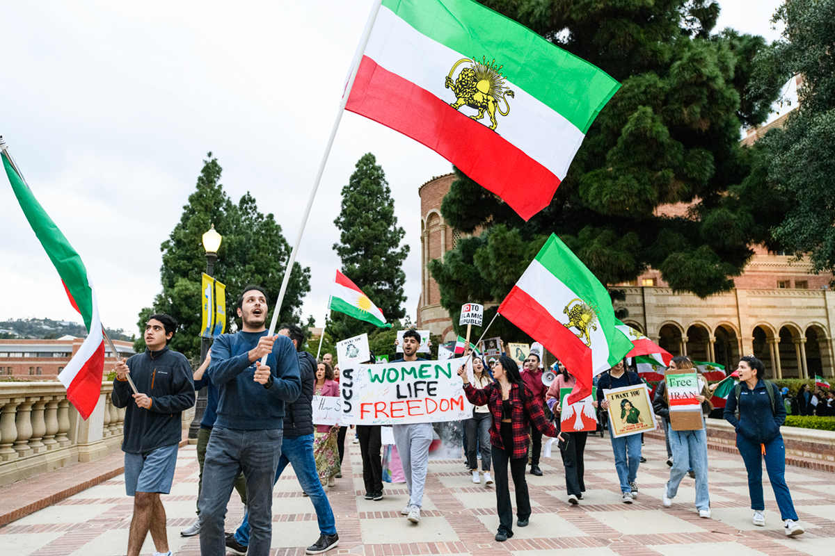 Students at a rally hold Iranian flags and signs advocating for women's rights and freedom.
