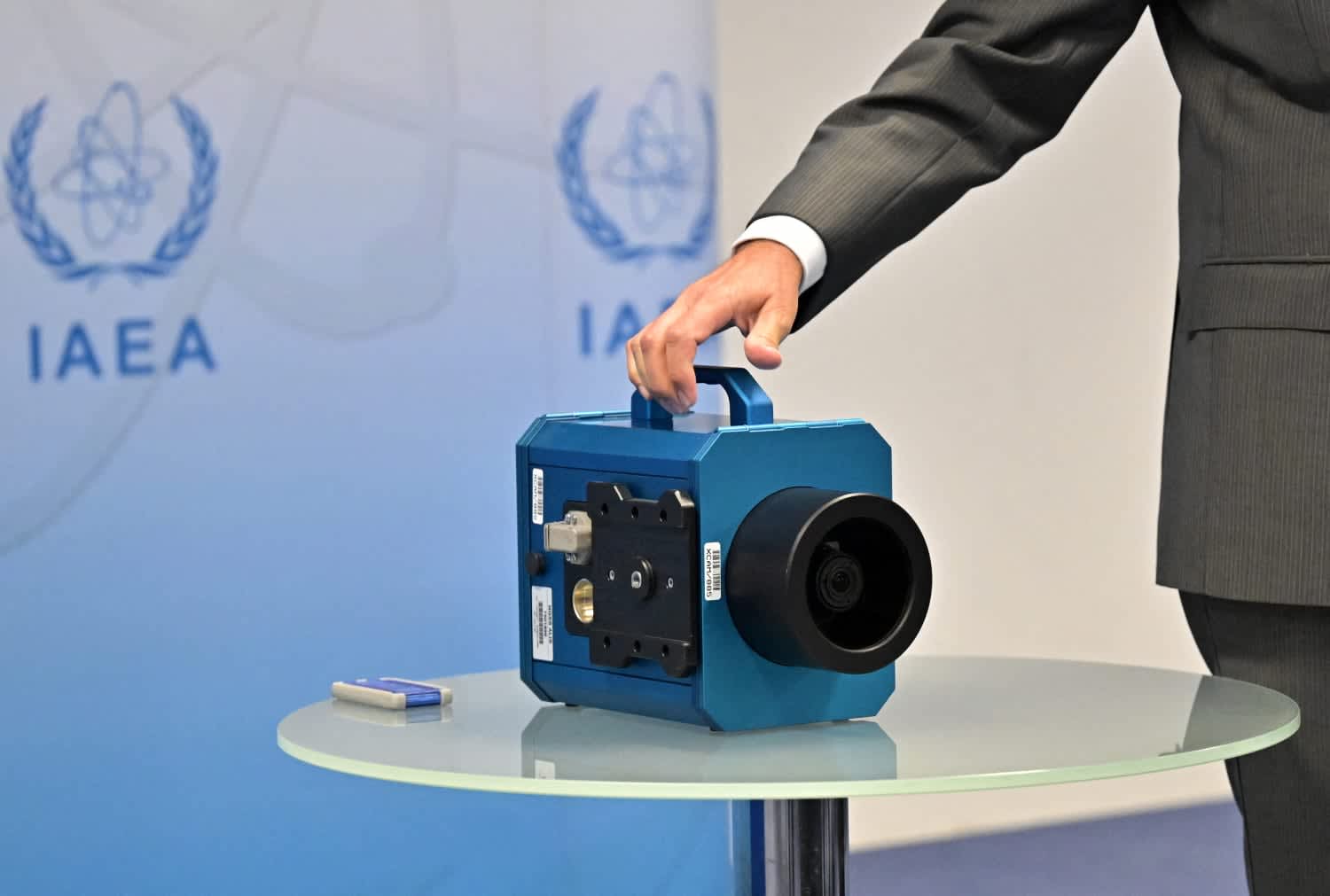 An IAEA official's hand holds a blue monitoring device, representative of equipment used for nuclear inspections.