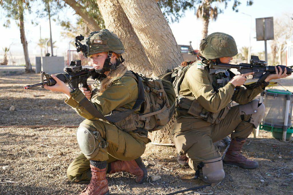 Israeli soldiers in tactical gear crouch with rifles during what appears to be a training exercise in an arid environment.