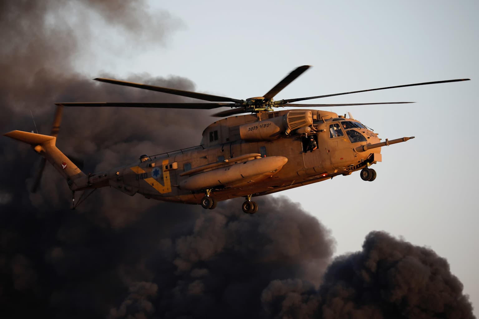 An Israeli Air Force CH-53 Yas'ur helicopter in flight amidst a backdrop of black smoke.