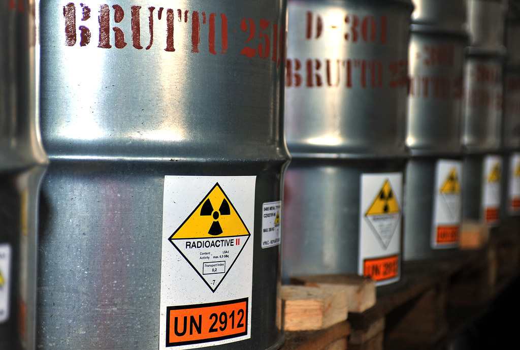 Metal drums labeled with radioactive symbols, containing yellowcake uranium concentrate, stored on wooden pallets.