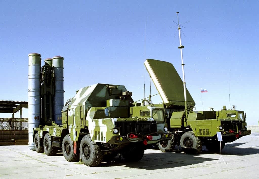 Components of a Russian S-300 air defense system, including a missile launcher and a radar vehicle, displayed outdoors.