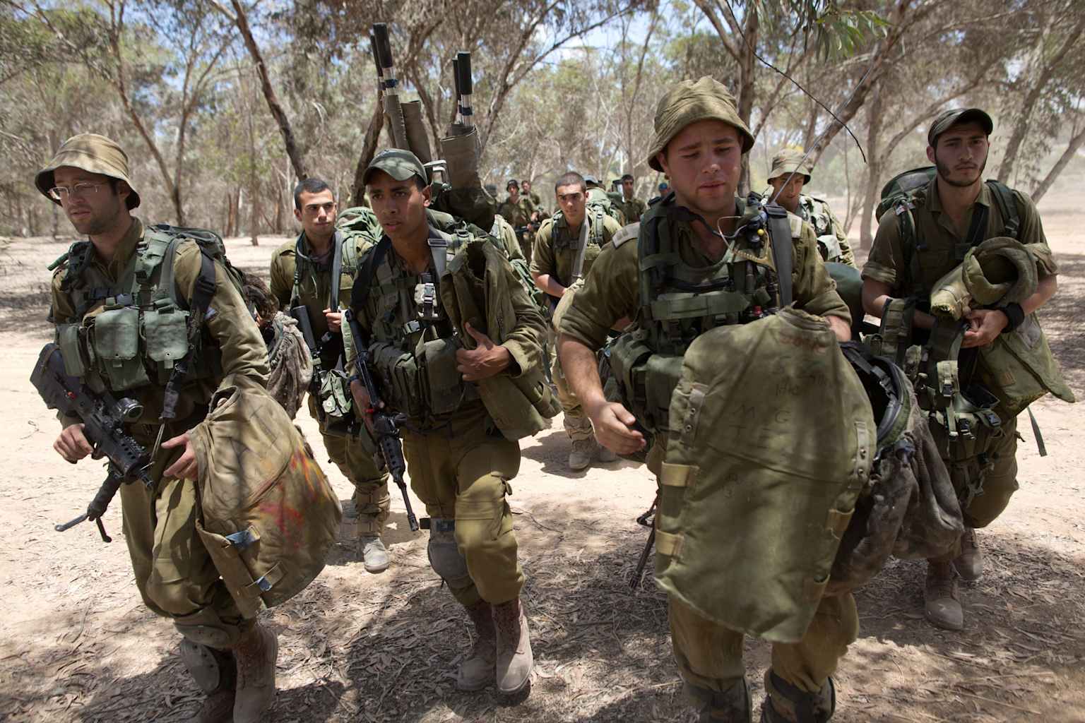 Israeli soldiers, equipped with tactical gear and rifles, move through a dry, wooded area during a training exercise.