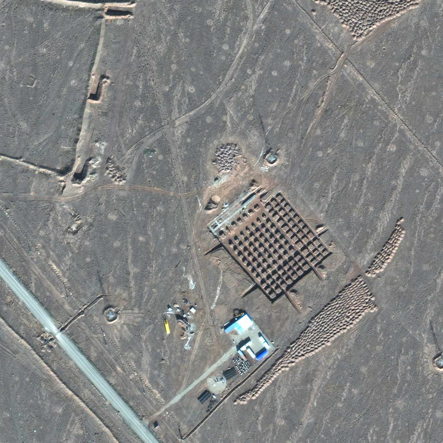 An aerial view of the Fordow nuclear facility, showing its distinctive grid-patterned underground structures and surrounding arid landscape.