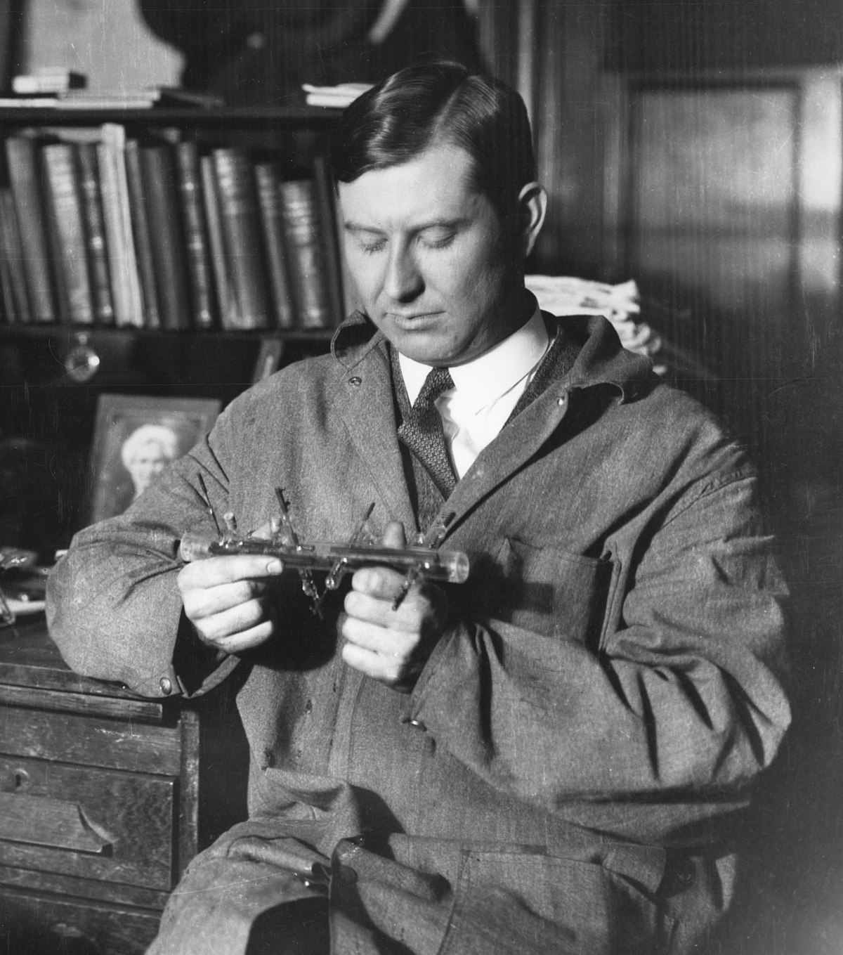 Physicist Jesse Beams examining a glass scientific apparatus, a field in which he was a pioneer.