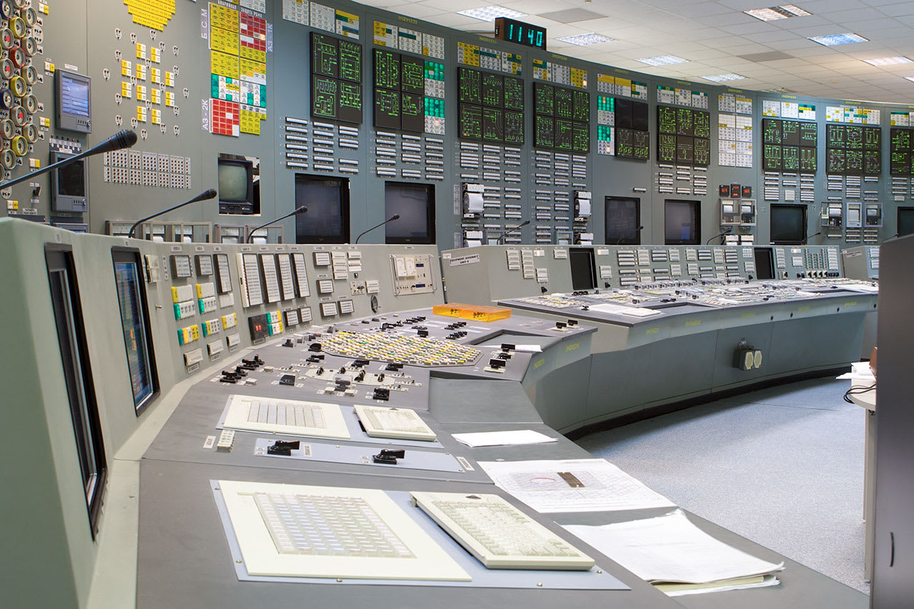 An interior view of a nuclear power plant control room, featuring numerous monitoring consoles and display panels for managing reactor safety systems.